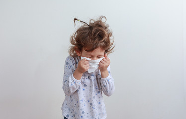 Young girl sneezing into a paper handkerchief in front of a white background.