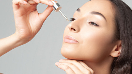 Young beautiful woman with clean perfect skin uses age-sensitive serum in pipette