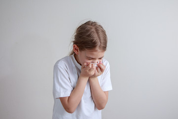 Young girl coughing into a paper handkerchief in front of a white background.