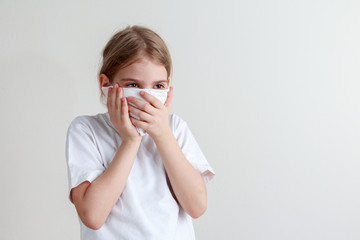 Young girl protecting herself with a paper handkerchief from germs and looking seriously in front of a white background.