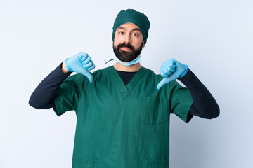 Surgeon man in green uniform over isolated background showing thumb down with two hands