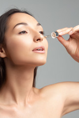 Fototapeta premium Young beautiful woman with clean perfect skin uses age-sensitive serum in pipette