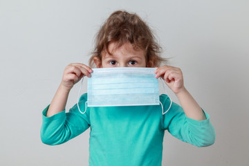 Young girl holding a medical mask, symbolizing protection from germs and looking seriously.