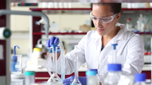 Researcher carrying out scientific experiment in a hi-tech chemistry laboratory. Analyzing results, sampling, pipet, mixing liquids in flasks. 