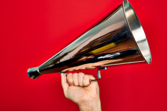 Beautiful hand of man holding vintage megaphone over isolated red background