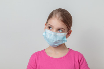 Young teenage girl protecting herself with a medical mask from germs and looking curiously and astonished.