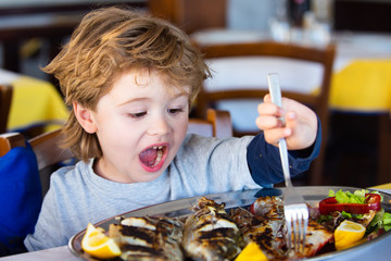 Excited child eats sea fish in a restaurant. Mediterranean diet. Healthy food for kids. Sea fish for lunch as a source of iodine. A child in a cafe is having lunch.