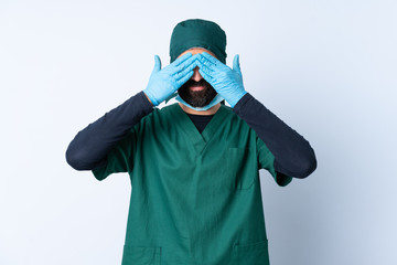 Surgeon man in green uniform over isolated background covering eyes by hands and smiling