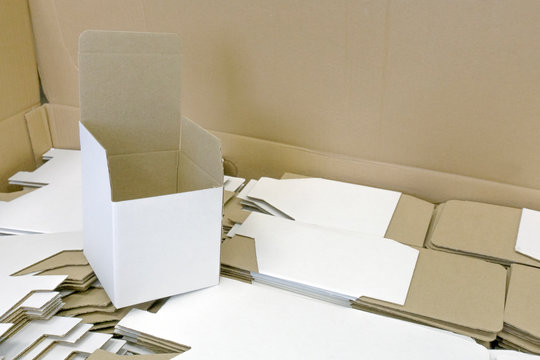 Folded cardboard box stands on disassembled. A lot of packaging for mugs. Disassembled condition, not folded. White color outside. Wholesale and retail trade. Production of souvenirs.