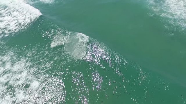 Aerial shot of a wave rolling into Big Bay during a sunny day in Cape Town slow motion