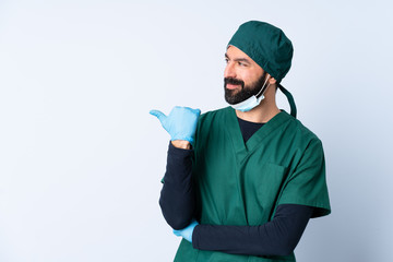 Surgeon man in green uniform over isolated background pointing to the side to present a product