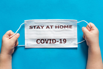 Children's hands hold a medical respiratory disposable mask for protection against viruses on a blue background with the inscription Stay at home