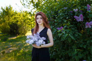 Portrait of woman holding lilac flowers bouquet on blossomig bush background