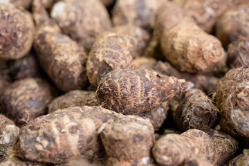 Pile of raw, unpeeled tropical Eddoe corms, Colocasia antiquorum, on a UK market stall
