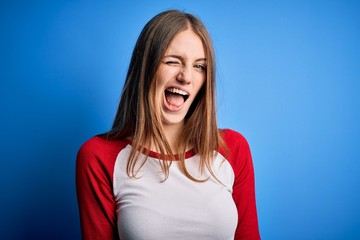 Young beautiful redhead woman wearing casual t-shirt over isolated blue background winking looking at the camera with sexy expression, cheerful and happy face.