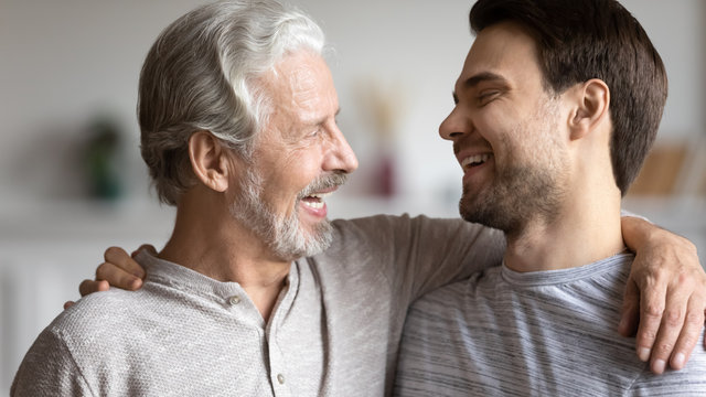 Happy young man hug elderly father have fun enjoying weekend at home together, smiling mature dad embrace grown-up adult son show pride and support, family bonding, parent kid relations concept
