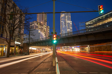 Night traffic on the german city street. Red and white light trails created due to long exposure. skyscraper, office buildings and a bridge in background, traffic light in the front, blue sky, dusk