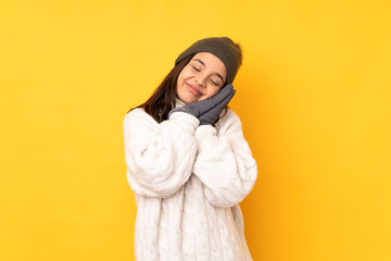 Young woman with winter hat over isolated yellow background making sleep gesture in dorable...