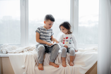 Brother and sister are sitting on the windowsill and reading a book. Happiness, family