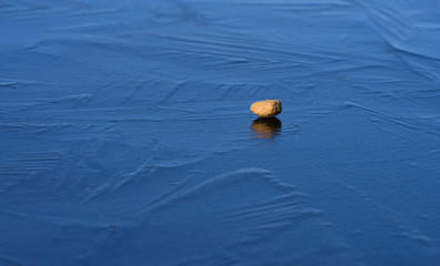 Kibble of dog dry food on blue ice. Light brown pellet reflecting from slippery surface. Ice pattern. Bright spring outdoor day. 