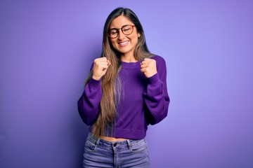 Obraz na płótnie Canvas Young beautiful smart woman wearing glasses over purple isolated background excited for success with arms raised and eyes closed celebrating victory smiling. Winner concept.