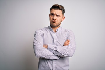 Young business man with blue eyes standing over isolated background skeptic and nervous, disapproving expression on face with crossed arms. Negative person.