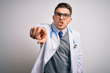 Young doctor man with blue eyes wearing medical coat and stethoscope over isolated background pointing displeased and frustrated to the camera, angry and furious with you