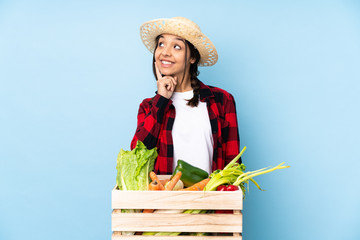 Young farmer Woman holding fresh vegetables in a wooden basket thinking an idea while looking up