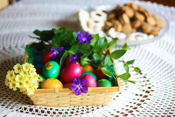 Easter colorful eggs, flowers and greens, white tea-set with eggs inside the cups with butterflies thin porcelain, on a white rounded knitted tablecloth. Country cozy style - happy holiday!