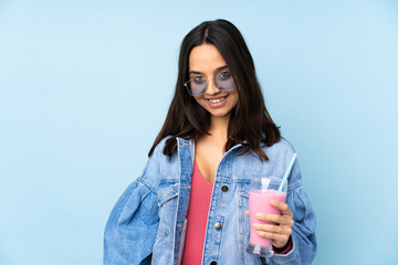 Young woman with strawberry milkshake over isolated blue background laughing