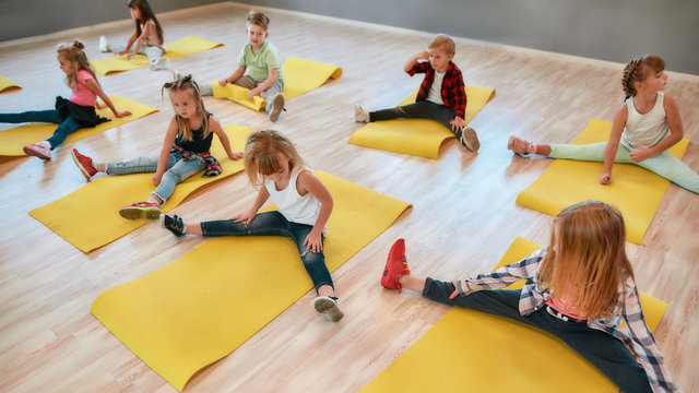 Flexible kids. Group of children sitting on the floor and doing gymnastic exercises in the dance studio. Physical education