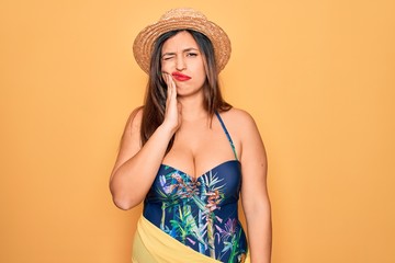 Young hispanic woman wearing summer hat and swimsuit over yellow background touching mouth with hand with painful expression because of toothache or dental illness on teeth. Dentist