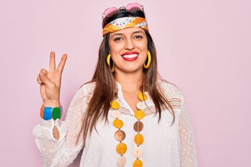 Young hispanic hippie woman wearing fashion boho style and sunglasses over pink background showing and pointing up with fingers number two while smiling confident and happy.