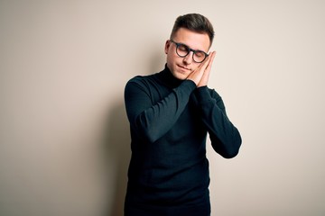 Obraz premium Young handsome caucasian man wearing glasses and casual sweater over isolated background sleeping tired dreaming and posing with hands together while smiling with closed eyes.
