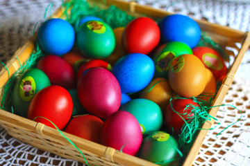 Easter colorful eggs, flowers and greens, white tea-set with eggs inside the cups with butterflies thin porcelain, on a white rounded knitted tablecloth. Country cozy style - happy holiday!