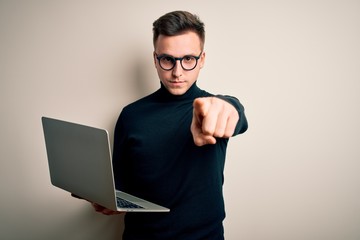 Young handsome caucasian business man wearing glasses using computer laptop pointing with finger to the camera and to you, hand sign, positive and confident gesture from the front