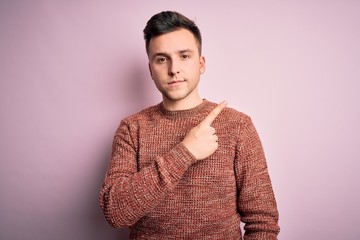 Young handsome caucasian man wearing casual winter sweater over pink isolated background Pointing with hand finger to the side showing advertisement, serious and calm face