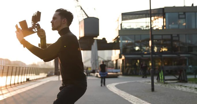 Filmmaker camera handheld on sunset in a big city. People run in background