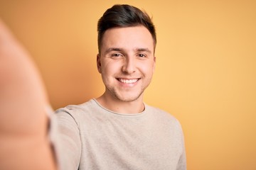 Young handsome caucasian man talking a selfie picture over yellow isolated background with a happy...