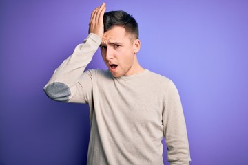 Young handsome caucasian man wearing casual sweater over purple isolated background surprised with hand on head for mistake, remember error. Forgot, bad memory concept.