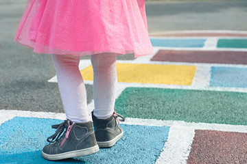 Closeup of girl's legs in a pink dress and hopscotch drawn on asphalt. Child playing hopscotch on playground outdoors on a sunny day. outdoor activities for children.