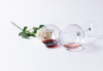 Couple of glasses with red and pink wine laying on white background, rose flower