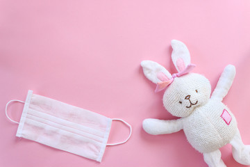 White toy rabbit with white mask and gloves on isolated pink background. Happy easter concept with coronavirus risk. Canceled easter.