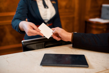 Here is your key. Close up of male and female hands. Smiling female receptionist behind counter in...