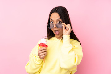 Young brunette girl holding a cornet ice cream over isolated pink background with glasses and...