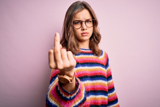 Young beautiful blonde girl wearing glasses and casual sweater over pink isolated background Showing middle finger, impolite and rude fuck off expression