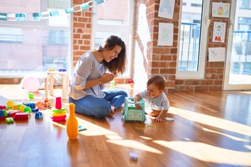 Beautiful teacher and toddler playing around lots of toys at kindergarten