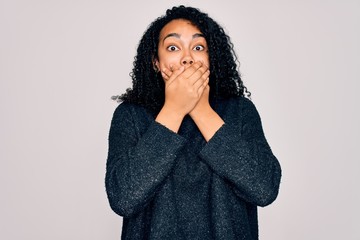 Young african american curly woman wearing casual sweater standing over white background shocked covering mouth with hands for mistake. Secret concept.