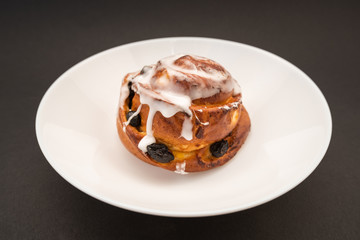 bun with raisins in white plate on black background