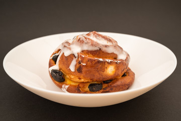 bun with raisins in white plate on black background